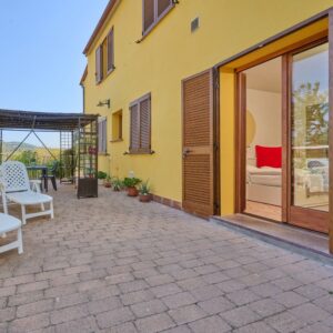 Facciata gialla del Monolocale di Meo a Suvereto con porta finestra aperta sulla camera da letto e terrazza pavimentata con sedie a sdraio