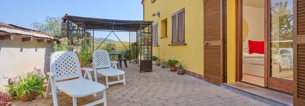 Ampia terrazza esterna in cotto del Monolocale di Meo nelle campagne di Prata, Suvereto, con piante in vaso e area relax per meditazione.