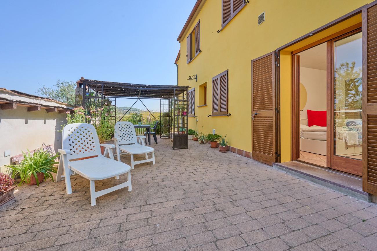Ampia terrazza esterna in cotto del Monolocale di Meo nelle campagne di Prata, Suvereto, con piante in vaso e area relax per meditazione.