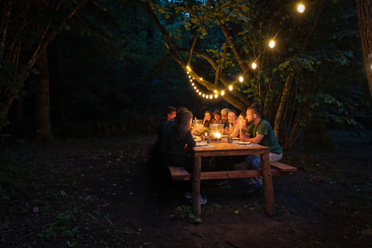 Un gruppo riunito intorno a un tavolo di legno nel bosco, illuminato da luci soffuse al Canyon Park.