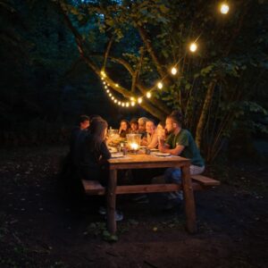 Cena conviviale sotto luci soffuse nel bosco al Canyon Park, con un gruppo di partecipanti riuniti intorno a un tavolo.