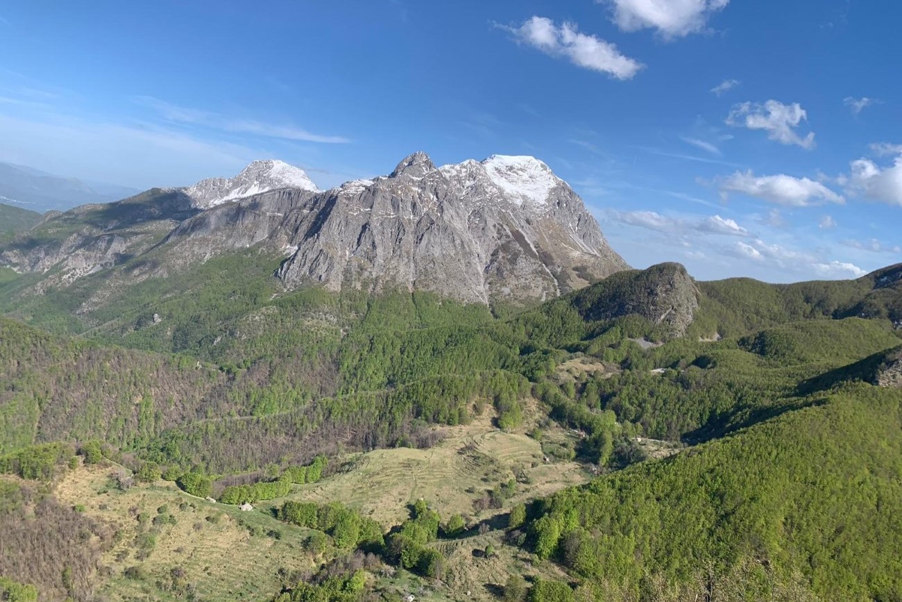Vista panoramica del Monte Sumbra e delle Alpi Apuane, circondati da una natura verdeggiante e cieli azzurri