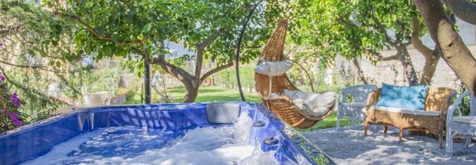 Jacuzzi esterna immersa nel giardino del B&B Il Giardino dei Limoni a Suvereto, circondata da alberi di limone, sedute in rattan e una poltrona sospesa