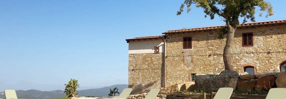 La piscina con acqua salata dell'agriturismo Poggio Belvento a Suvereto, con il casolare in pietra e la vista sulle colline della Maremma Toscana.