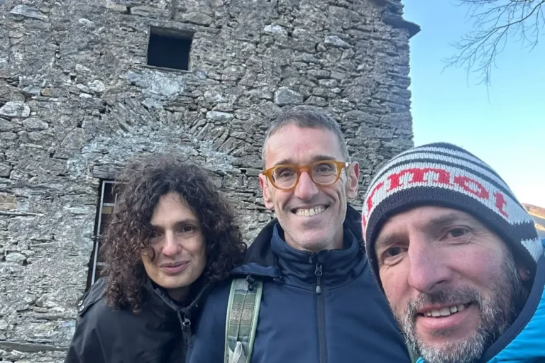 Selfie di Gianni e Patrizia di Vacanze Sportive Toscana con la guida AMM Luigi Lorenzoni davanti a un rustico in pietra durante un trekking invernale sulle Alpi Apuane.