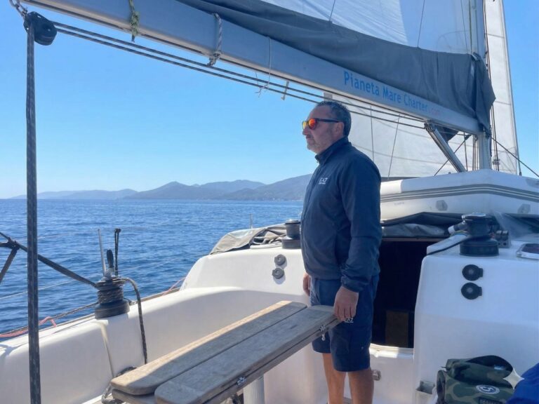 Andrea Calestrini, fondatore di Pianeta Mare Charter, sorridente a bordo di una barca a vela nel porto di Piombino. L'immagine accompagna la sua storia sul cambio di vita per dedicarsi alla vela.