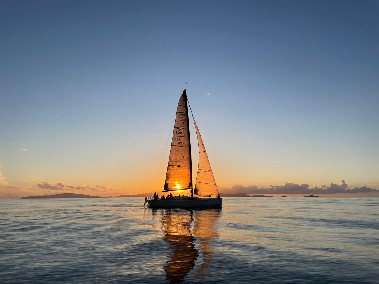 Una barca a vela della flotta Pianeta Mare Charter naviga al tramonto nel mare della Toscana. Questa immagine rappresenta la sensazione di libertà e il colpo di fulmine per la vela di Andrea Calestrini.
