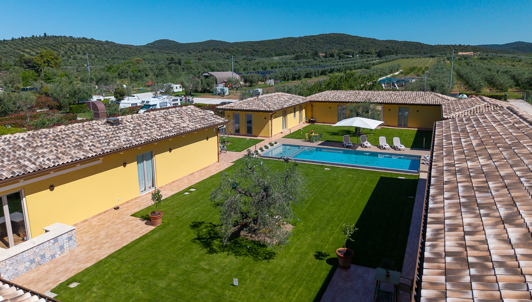 Veduta aerea dell'azienda agricola Agricoccinella a Riotorto: in primo piano il cortile dell'agriturismo con piscina, sullo sfondo l'area agricampeggio tra gli ulivi della Maremma.